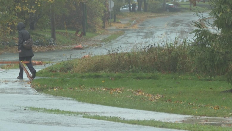 A person walking across a road filled in the rain.