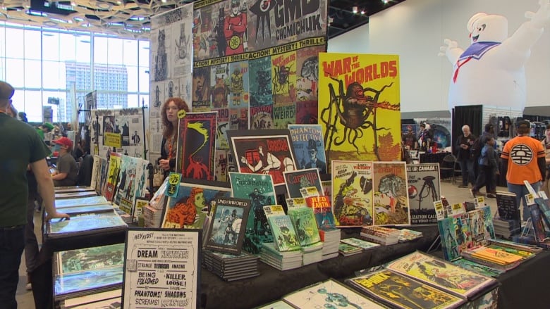 A person stands behind a booth selling comic books at Comiccon. 