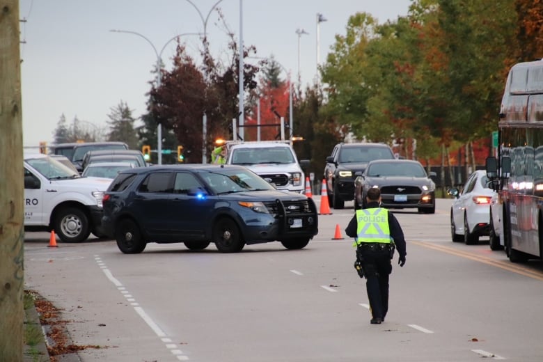 A police officer in a green reflective jacket walks in the middle of the road with busy traffic.