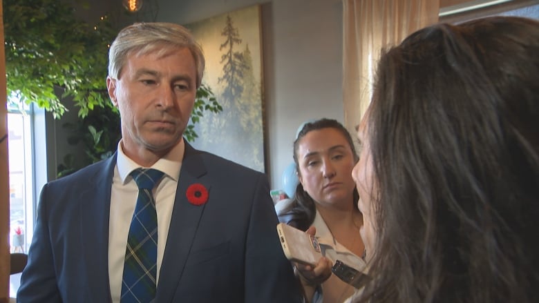 a man wearing a suit looks at a woman who is close to the camera, asking questions. 