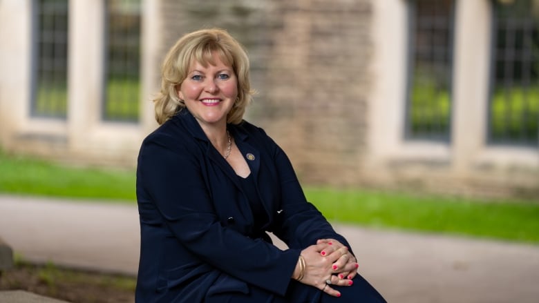 A portrait of a person in business clothes seated outdoors. 