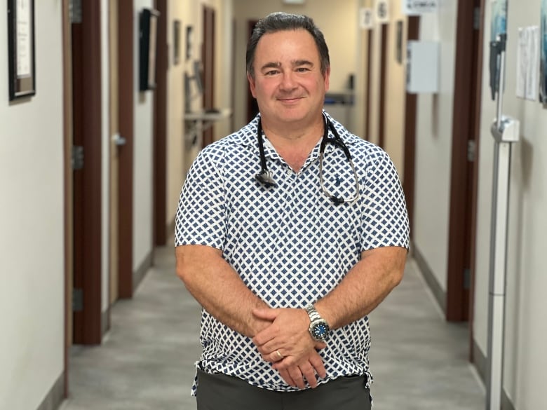 A portrait of a man with dark hair standing in a hallway with a stethoscope around his neck. 