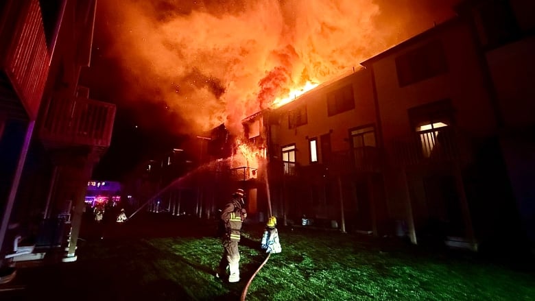 Two firefighters spray water on a raging townhouse fire.