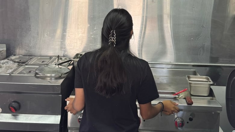 A young woman stands in a kitchen, with her back to the camera.