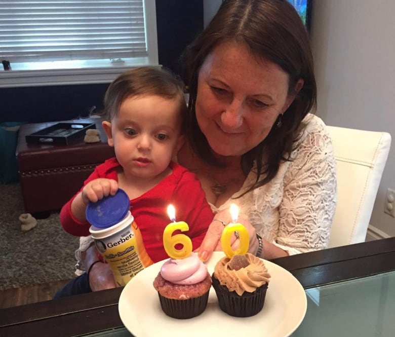 A woman with a toddler on her lap blows out the candles on two cupcakes.