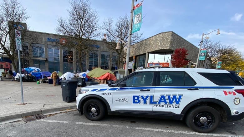 A City of Guelph bylaw SUVis parked near a tent encampment at in downtown city square