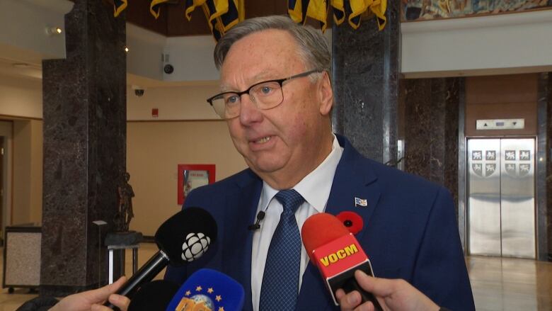 A man in a blue shit standing behind three microphones. 