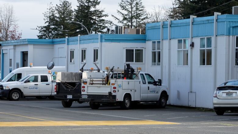 A number of blue and white construction trailers are seen side by side with public works trucks parked in front of them.