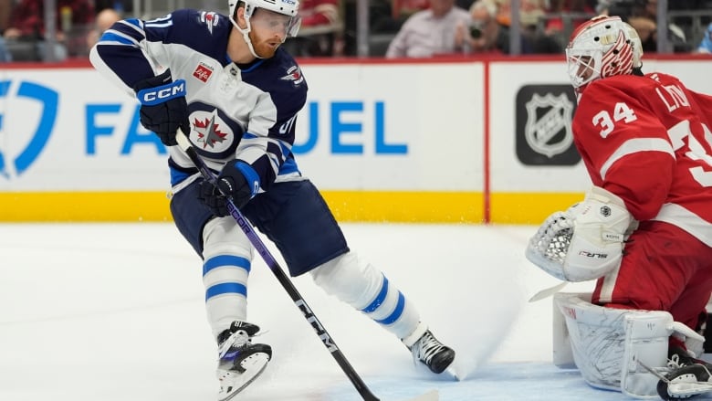 A hockey player has his stick on the puck as he approaches a goalie at the net.