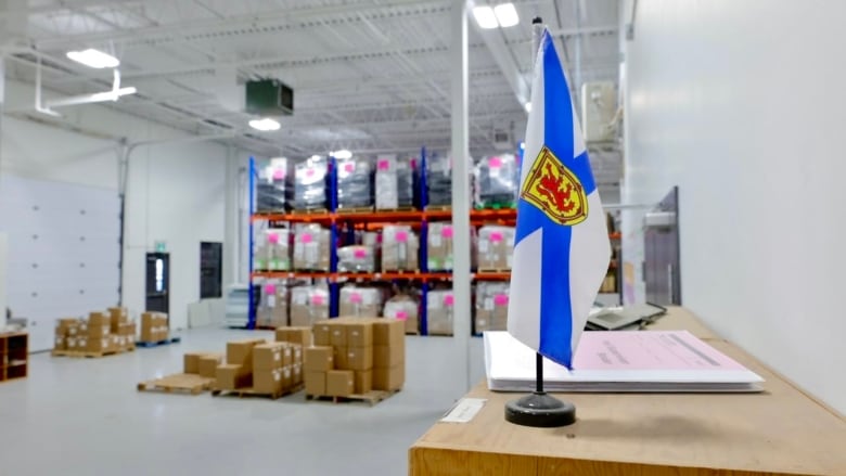 A small Nova Scotia flag sits on a desk in a warehouse full of boxes.