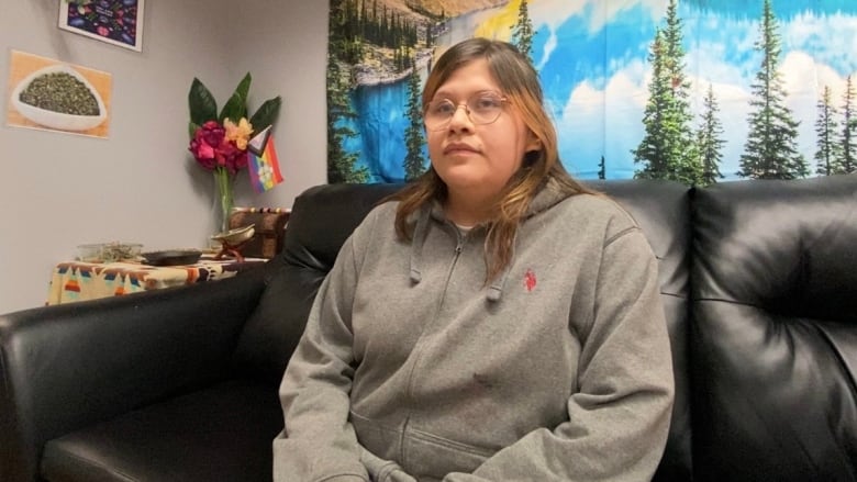 A young girl wearing glasses and a grey sweater sitting on a couch. 