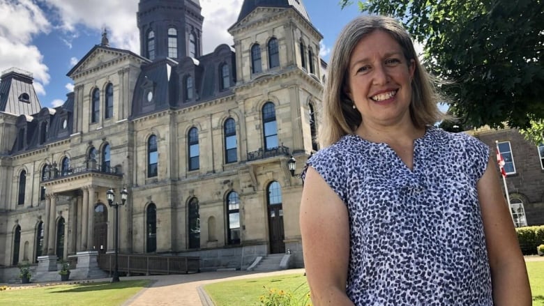 A wioman in a short-sleeved flowered blouse stands outside infront of the New Brunswick legislature.