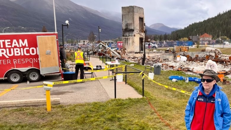 Man stands near burned-down building.