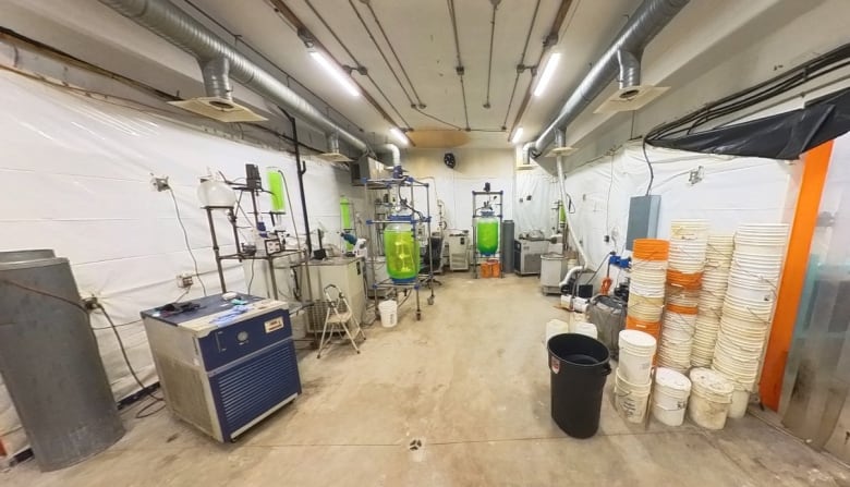 The interior of what looks like a lab with various containers and machines on a wooden floor under large hood vents and fluorescent lights.