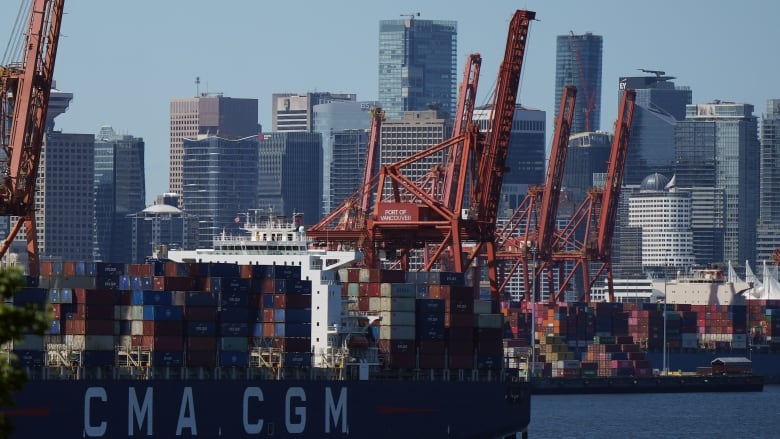 A large ship-unloading crane or gantry sits on the docks facing the water with the City of Vancouver skyline behind it.