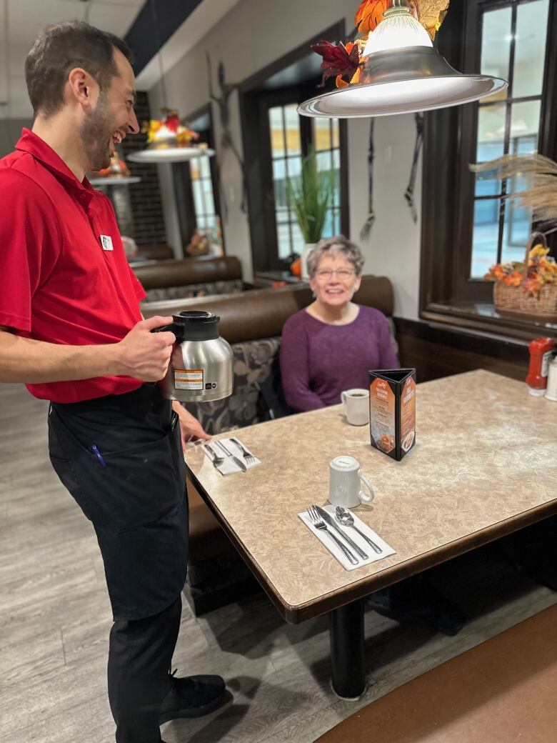 A waiter holding a coffee pot laughs alongside a customer.