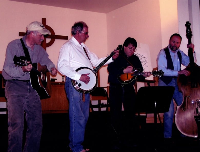 Four men in a bluegrass band perform on a stage.