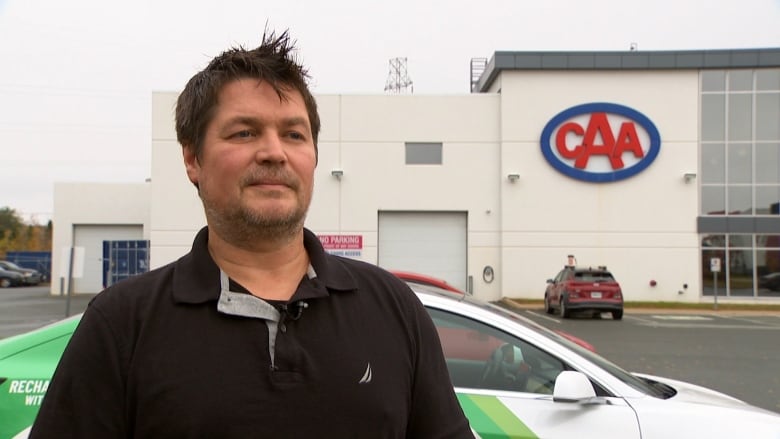 Kurt stands outside next to electric vehicle. 