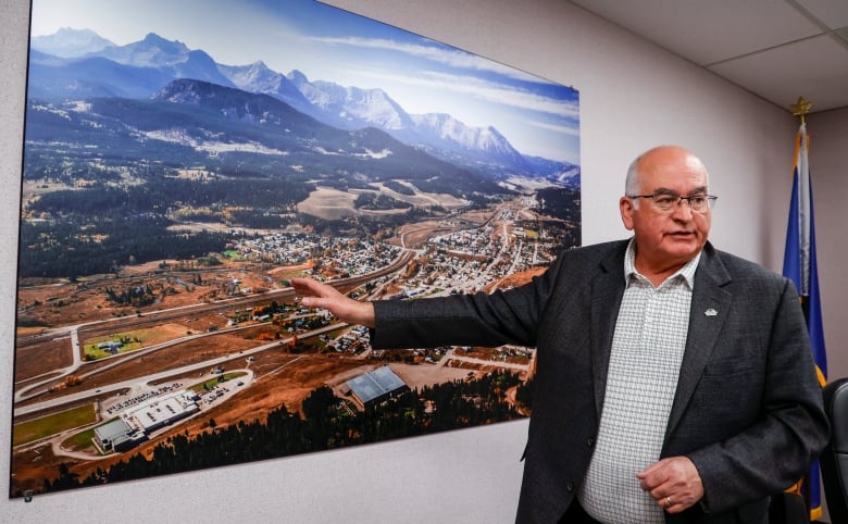 A man gestures at a highway map on the wall behind him.