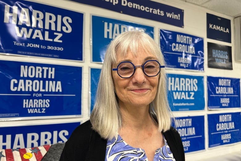 A person standing in front of a wall adorned with political signs smiles while posing for the camera.