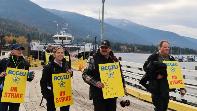 A group of workers walk off a ferry with sandwich boards reading 'BCGEU on Strike.'