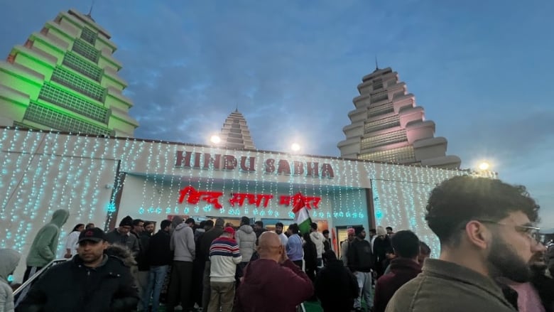 A crowd of people stand outside a Hindu temple on a dark fall evening