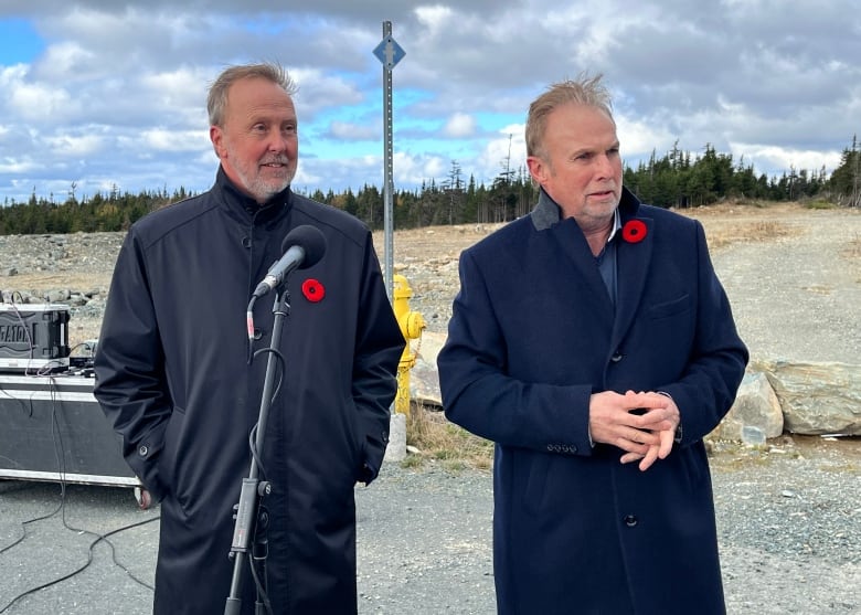 Two men wearing coats and a poppy flower are standing next to each other. 