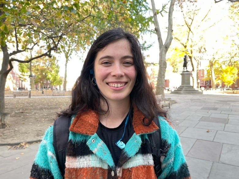 A woman wearing a colourful jacket smiles in a park.