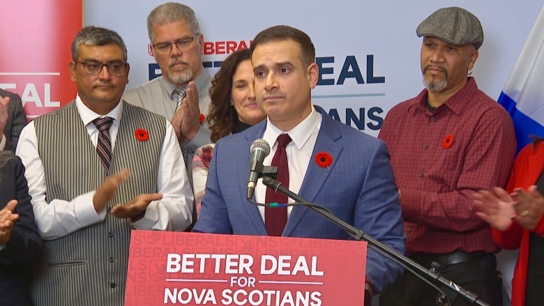 A man in a suit and tie stands at a podium with people behind him.