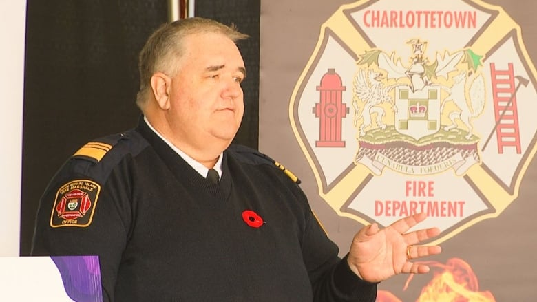 Man speaking in front of Charlottetown Fire Department logo. 