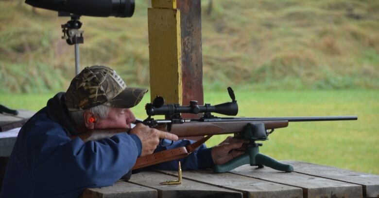 A hunter wearing earplugs points a rifle at a target