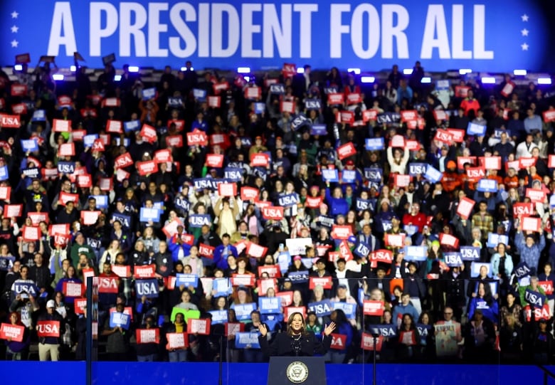 Kamala Harris speaks at a podium in front of a crowd of supporters under a banner reading 'A President For All.'