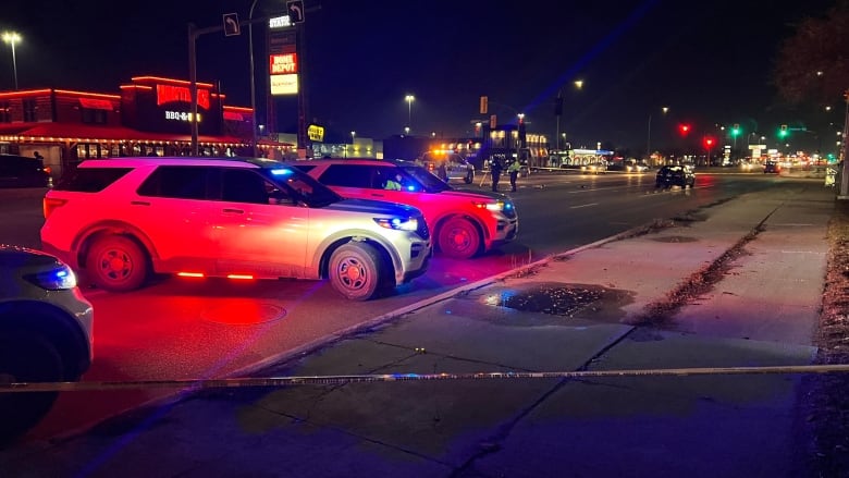 Police officers place evidence markers on a roadway near unmarked police vehicles. 