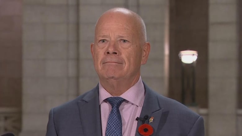 A man wearing a suit stands expressionless inside the rotunda of the Manitoba Legislature.