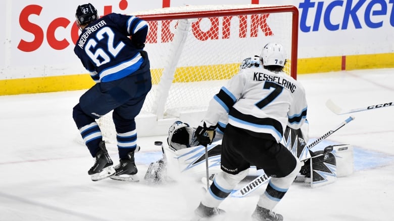 A player in blue wearing No. 62 slides the puck past the outstretched arm of a goaltender in white.