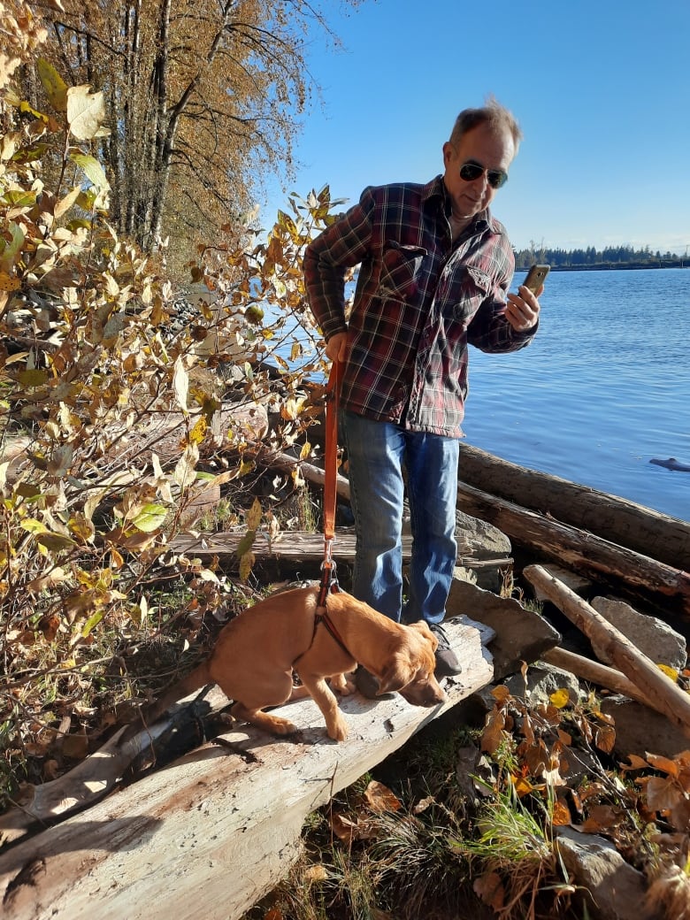 A man holds a dog by a leash near a river.