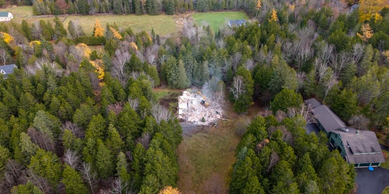 Aerial shot of a pile of rubble surrounded by trees and very few houses. 