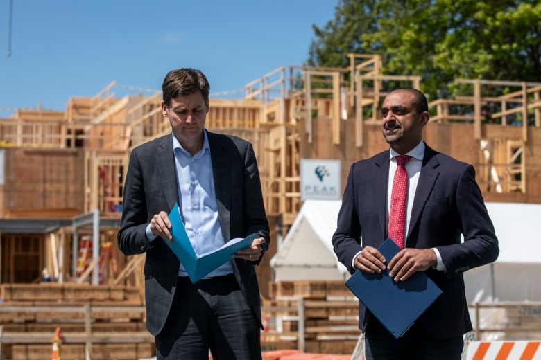 Two tall men are pictured with files in front of an under-construction home.