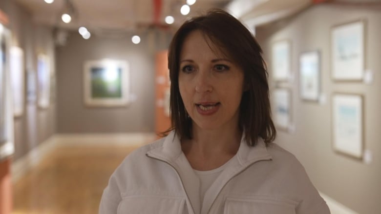 A woman on a white shirt stands in front a room. 