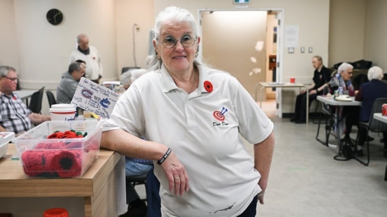 A woman poses in a room next to a basket of poppies and other legion members. 