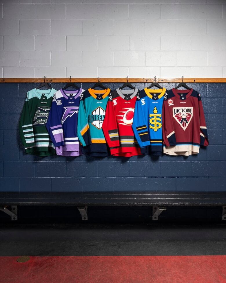 Six hockey jerseys are hung on the wall of a hockey dressing room.