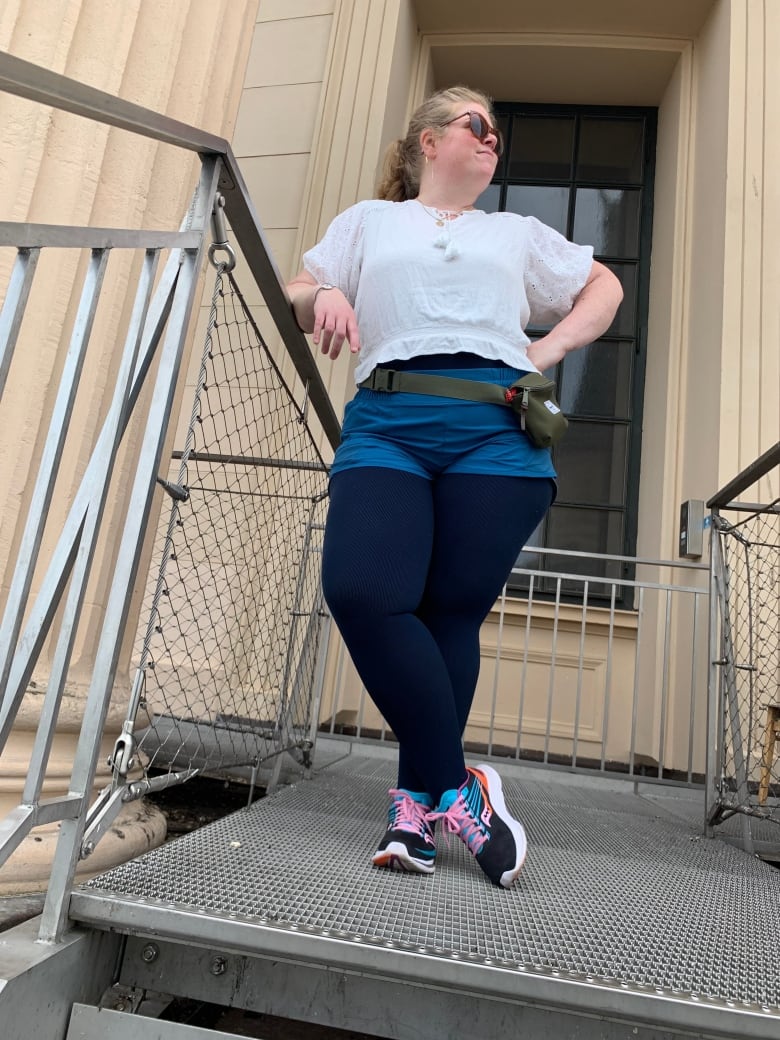 A woman is shown looking happy and confident, as she leans against a metal railing with her other hand on her hip.