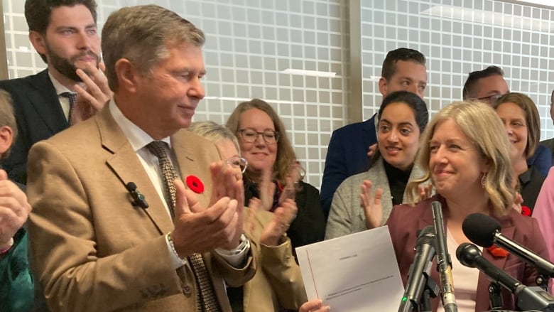 A group of people stand behind a microphone. One of them is holding up a document.