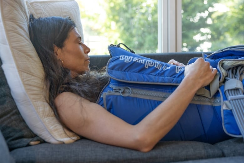 A woman is shown sleeping in a blue inflatable suit on a couch.