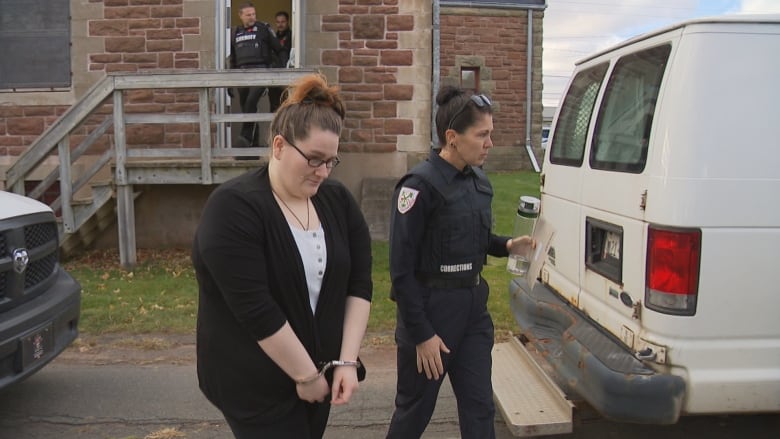 A woman in shackles is led from a courthouse to a police vehicle.