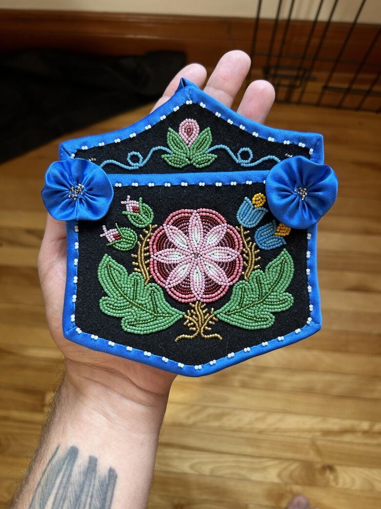 Hand holding a black pocket, that is trimmed in shiny blue material. There is floral beadwork on the pocket. 