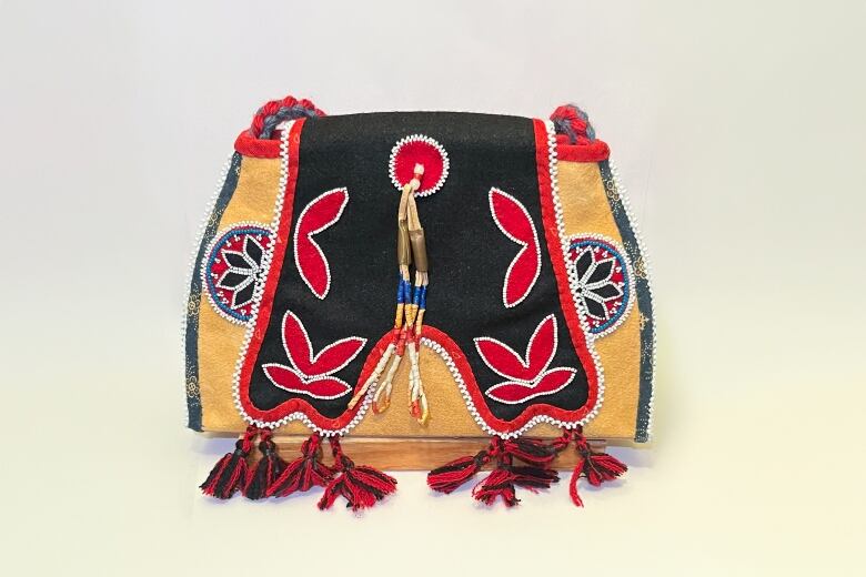 A brown leather bag, that has black, red, and blue beadwork on it. 