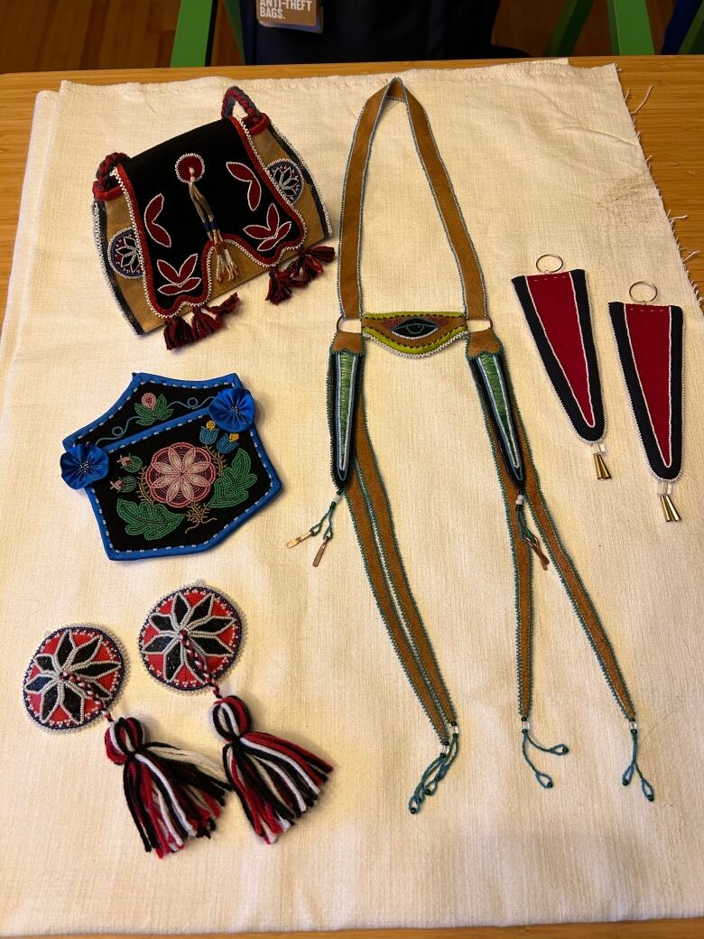 Beaded artwork sitting on a table, including a bag, a wall pocket, a horse headstall, earrings, and nipple pasties. 