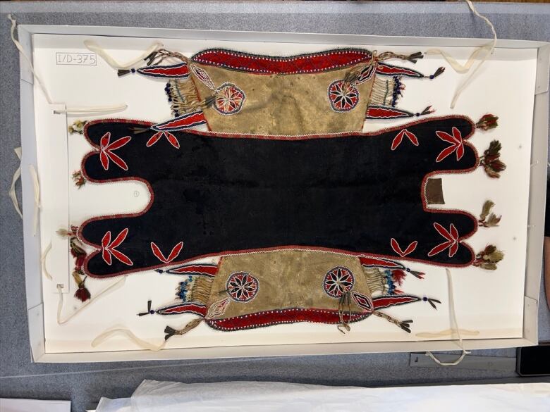 A brown leather pad saddle, decorated with patterns made out of red and black wool, and beads. 