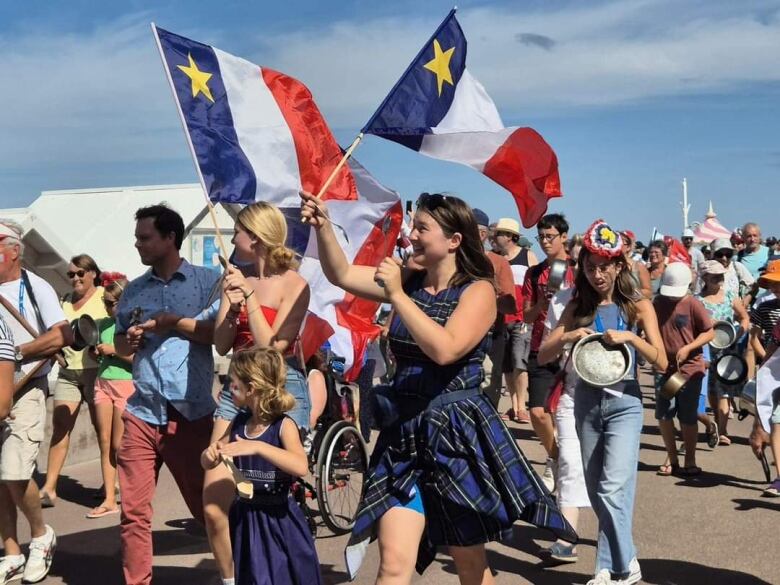 Karine Gallant and her children walk in a parade holding Acadian flags.